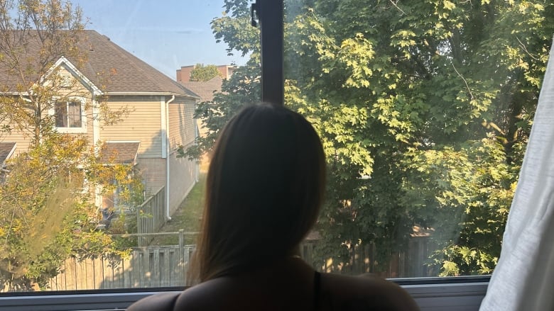 The mom of a sexual assault victim stands in front of the window through which her assailant is believed to have come in. She is in shadow to not identify her. 