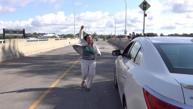 A woman celebrates as she walks back to her vehicle parked on a bridge.