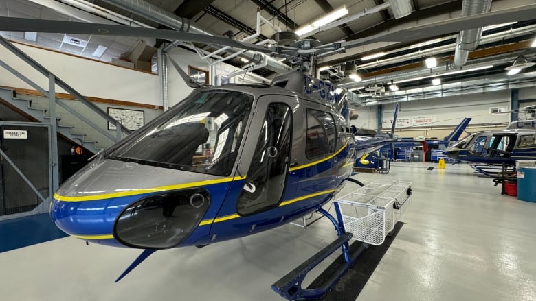 A shiny blue, gray and yellow helicopter is shown in a garage.