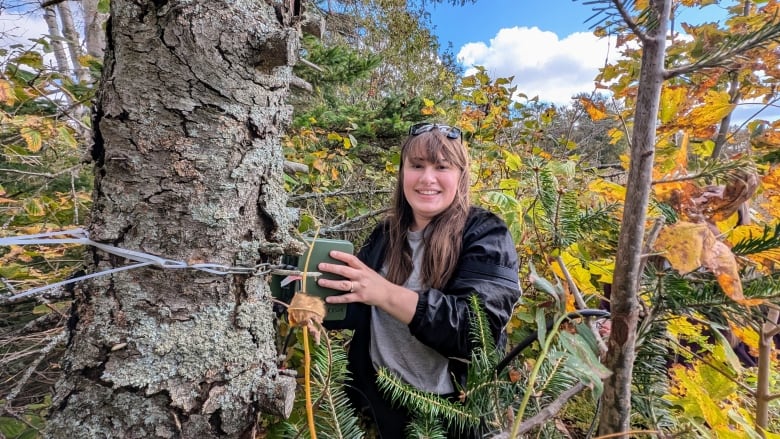 A woman next to a tree holding a small device 