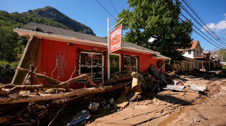 A red building with rubble and fallen tree branches in front of it is visible. Farther down the road, more rubble is visible. 