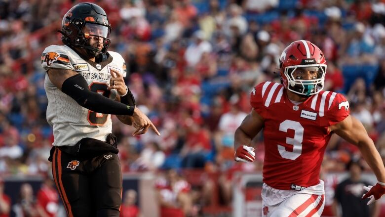 Two football players, one wearing black and white and the other wearing red and white, run.