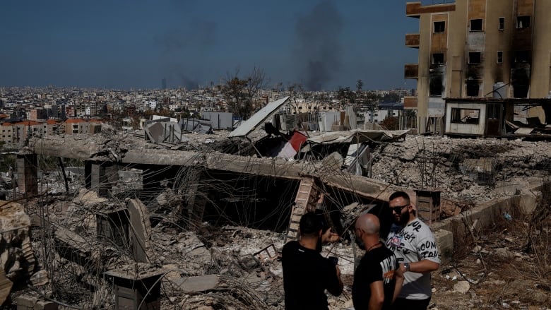 Three men stand amid the rubble of a destroyed building in Beirut.