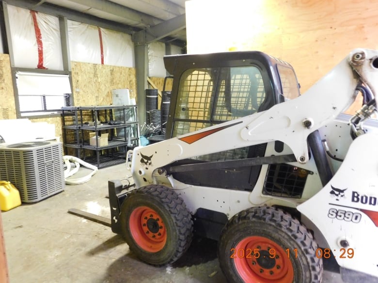 A white, black and red Bobcat skid-steer loader parked in a room. 