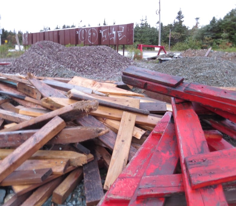 A pile of wooden planks, some painted red, with nails sticking out.