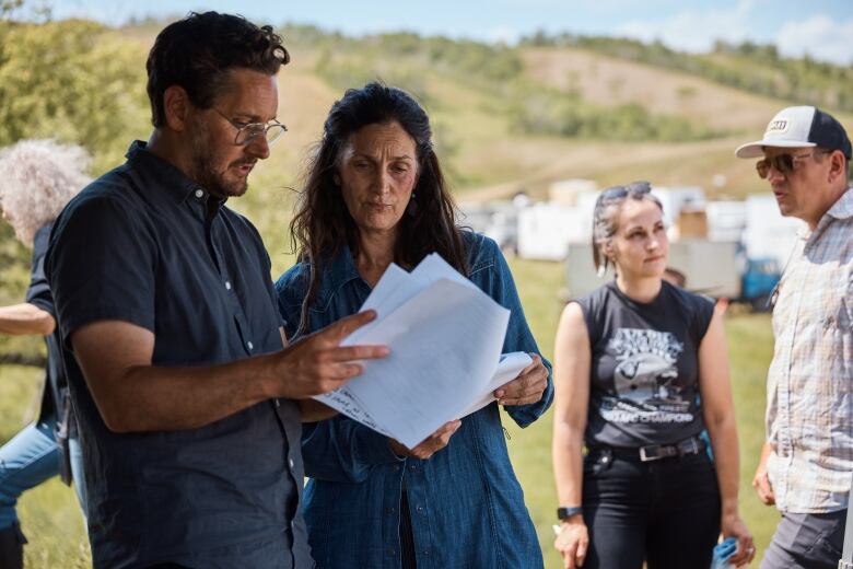 A man reads a script with a woman in the outdoors.