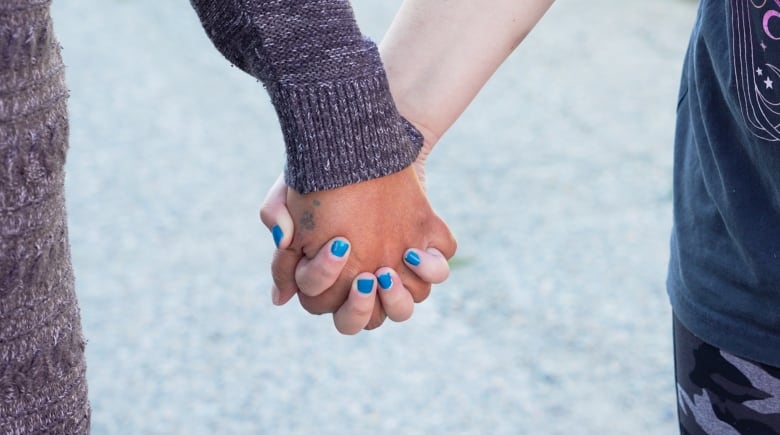 Two hands are seen clasped together, one of them with its nails painted blue.