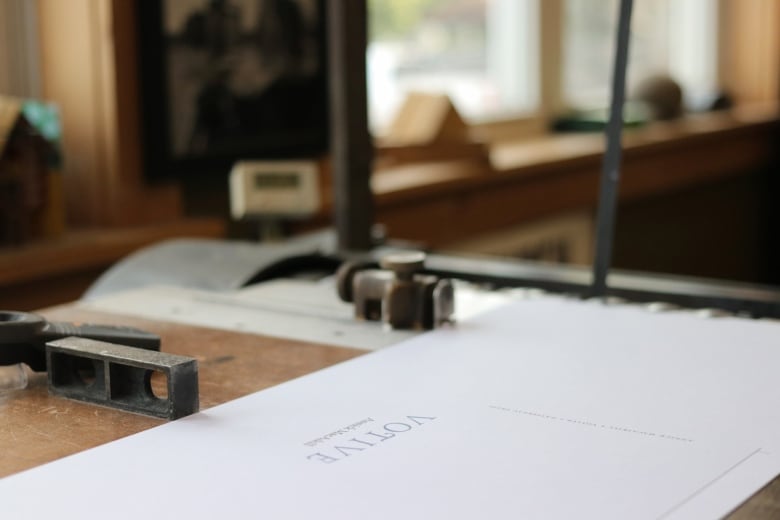 A book jacket sits atop a flat wooden surface. Windows are behind shining light.