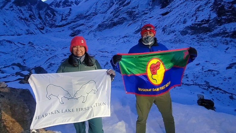 Two people are seen at the base of a mountain, holding signs.