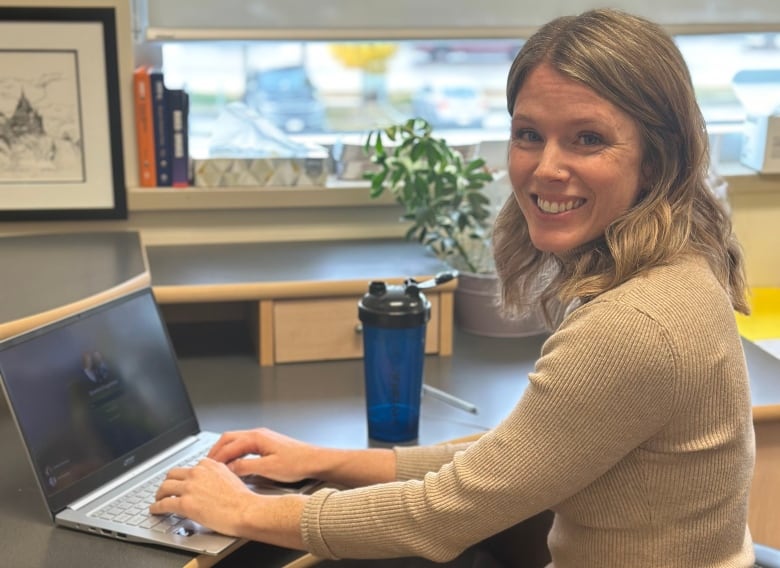 A woman sits at her computer and smiles at the camera.