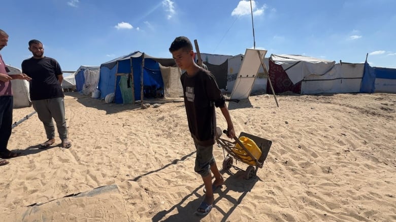 A boy pulls a cart with a yellow jug of water.