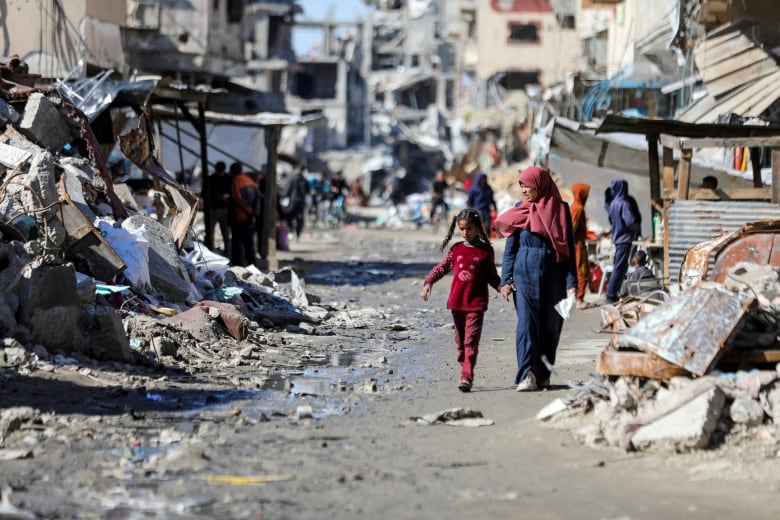 People walk past the ruins of houses.