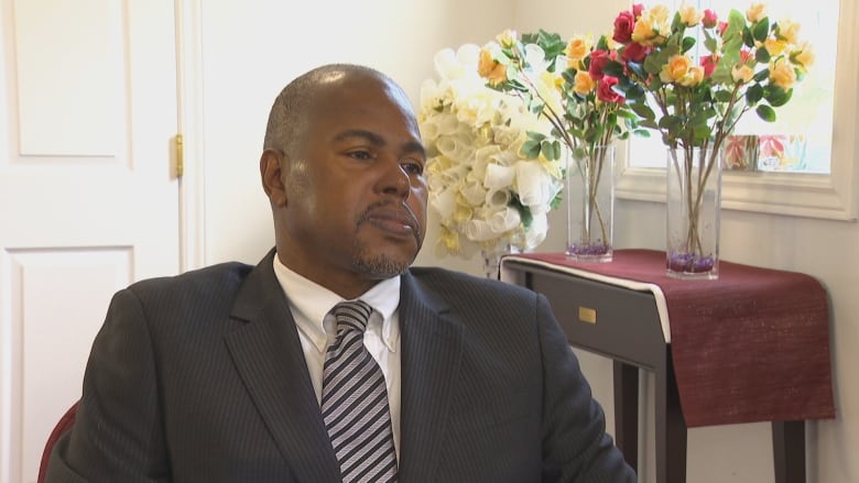 Man in suit sits near a table with vases of flowers in them