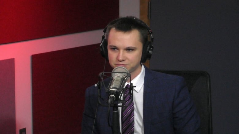 A man wearing a suit and black headphones sits at a microphone.