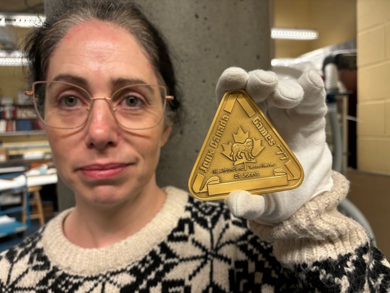 A woman holds up a triangular gold medal.