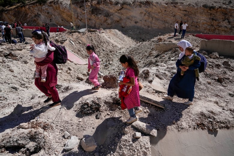 People walk over a rocky landscape with luggage.