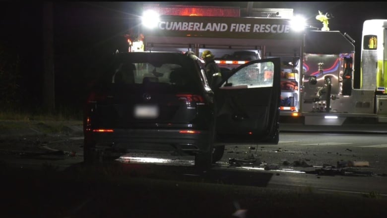 A scene of crash with a car with one of its door open and debris on the road with a fire truck in the background. 