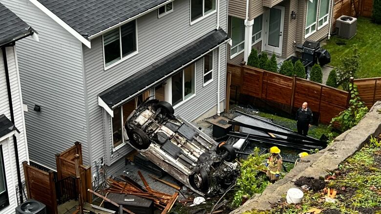 A scene of a crash showing a vehicle on its roof that crashed into a residence.