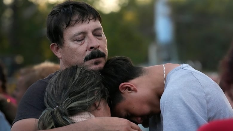 A man hugs two other people with his eyes closed.