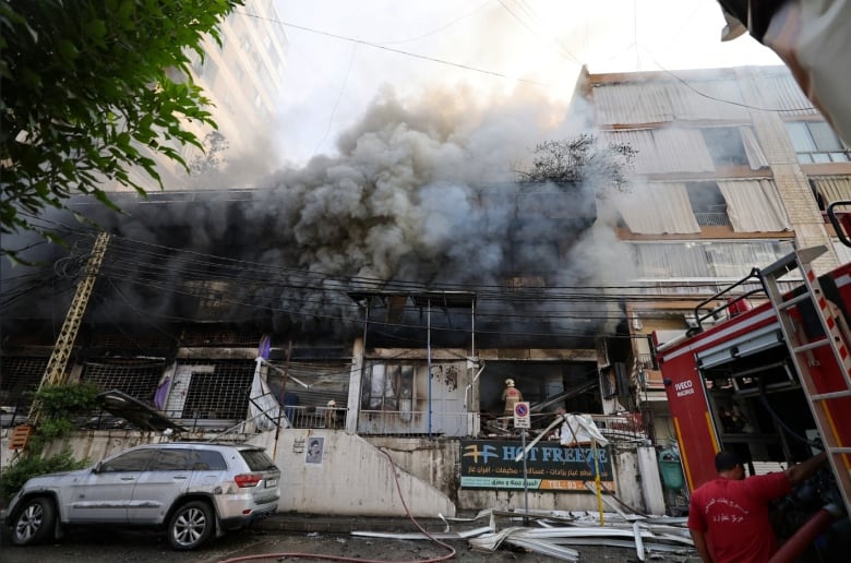 A firefighters enters a building which has black smoke rising from it.