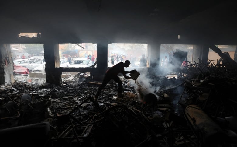 A person pours liquid on smouldering debris inside a heavily damaged building.