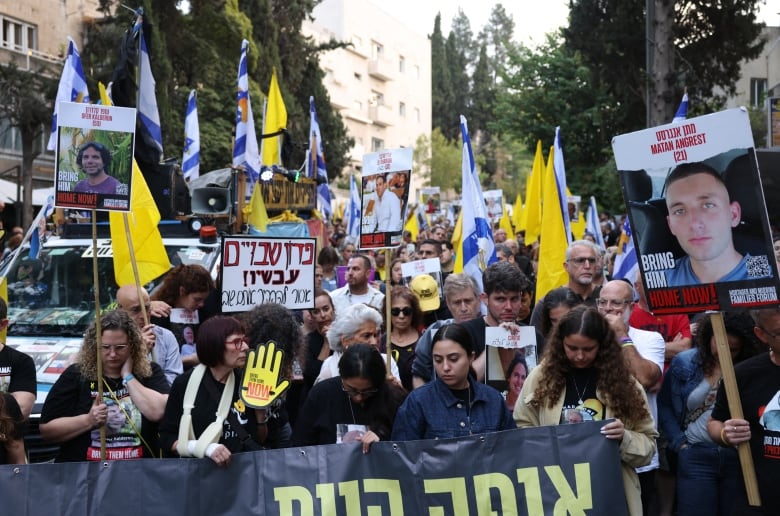 Dozens of people carrying banners and signs and flags are shown in a city street.