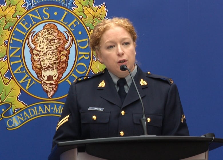 A uniformed police officer speaks into a microphone at a lectern. The RCMP logo is behind her. 