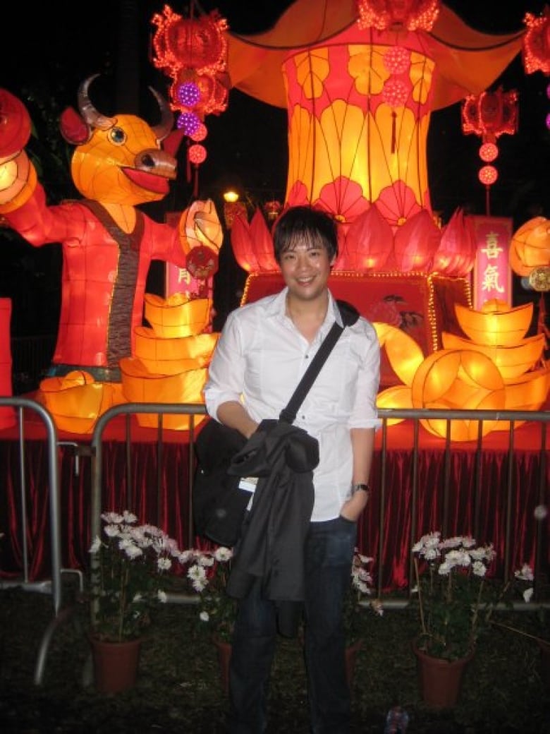 An Asian man carrying a shoulder bag smiles while posting in front of a colourful display