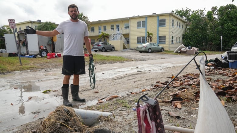 A man stands in a muddy street gesturing at debris