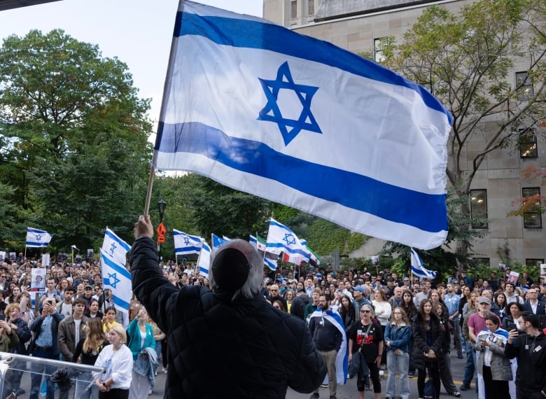 A man holds up an Israeli flag infront of a crowd of people. 