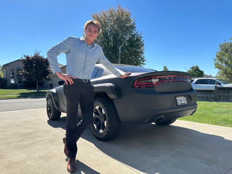 A young man leans against his muscle car.