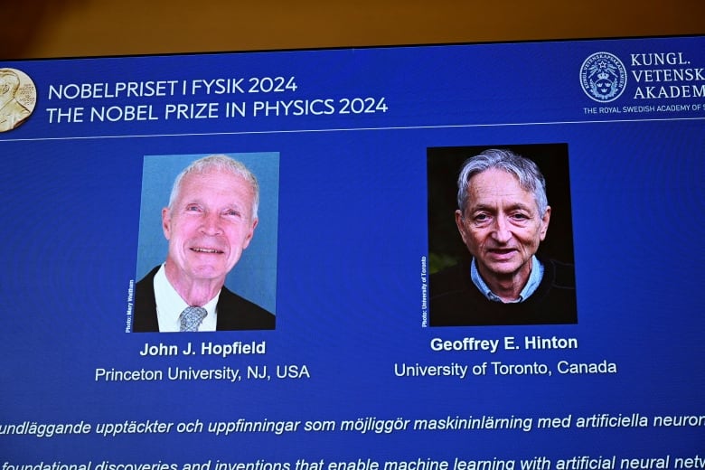 Two older men are shown on a video projection in a room during a presentation.