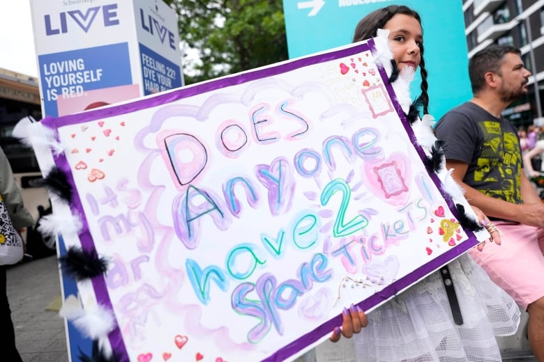 A girl holds a hand-made sign that says 