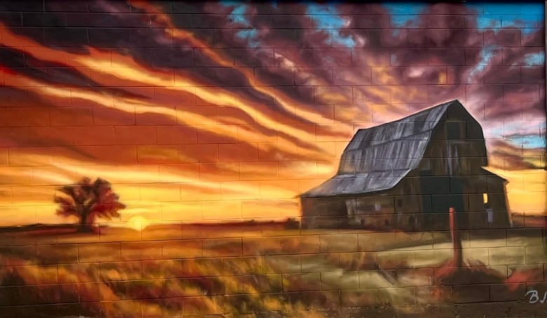 A mural by BJ Zieger shows an old farm building lit by the rays of a sinking sun.