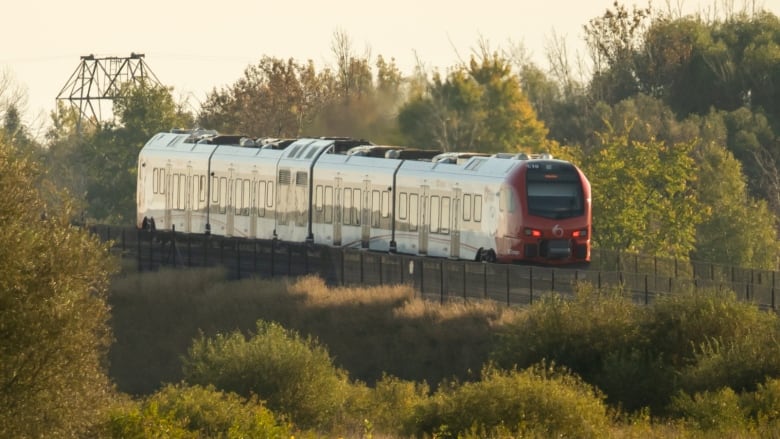 A public transit train on a rural section of track on a sunny autumn morning. 