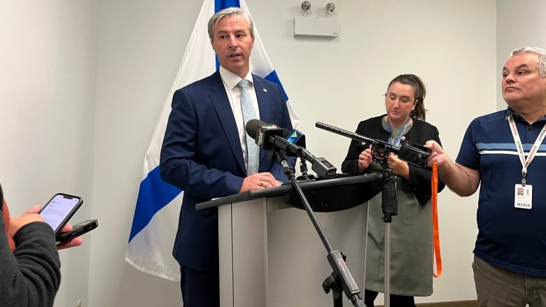 A man in a suit and tie stands at a podium in front of a Nova Scotia flag.