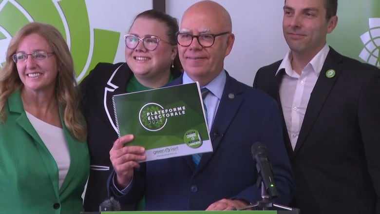 A man holding up a booklet while smiling with a group of others behind him