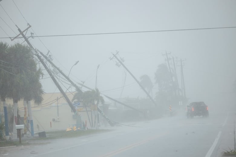 A pickup drives past broken utility poles downed by strong wind gusts