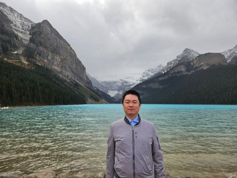 A man stands in front of an alpine lake.