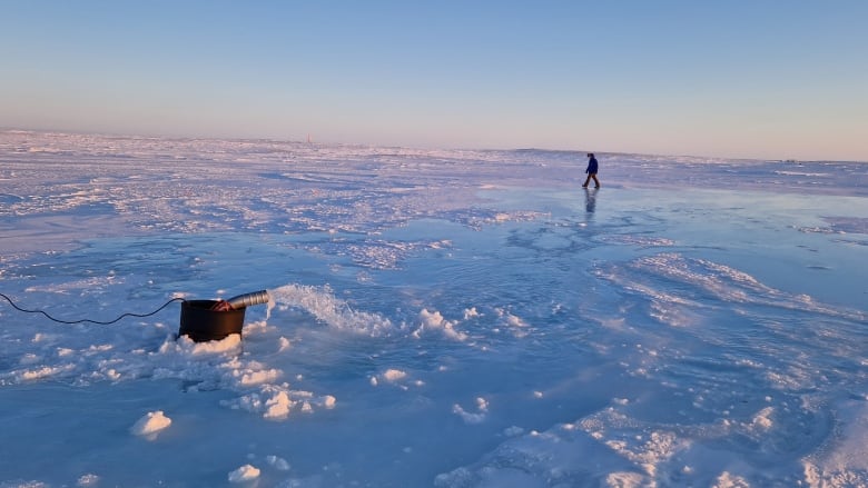 Man walks across frozen ocean surface in background. Pump with water gushing out in the foreground