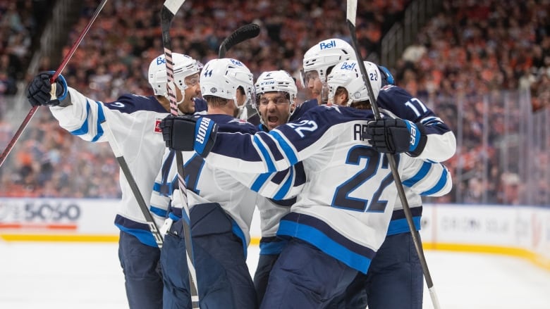 Five hockey players in white come together for a celebratory group hug.