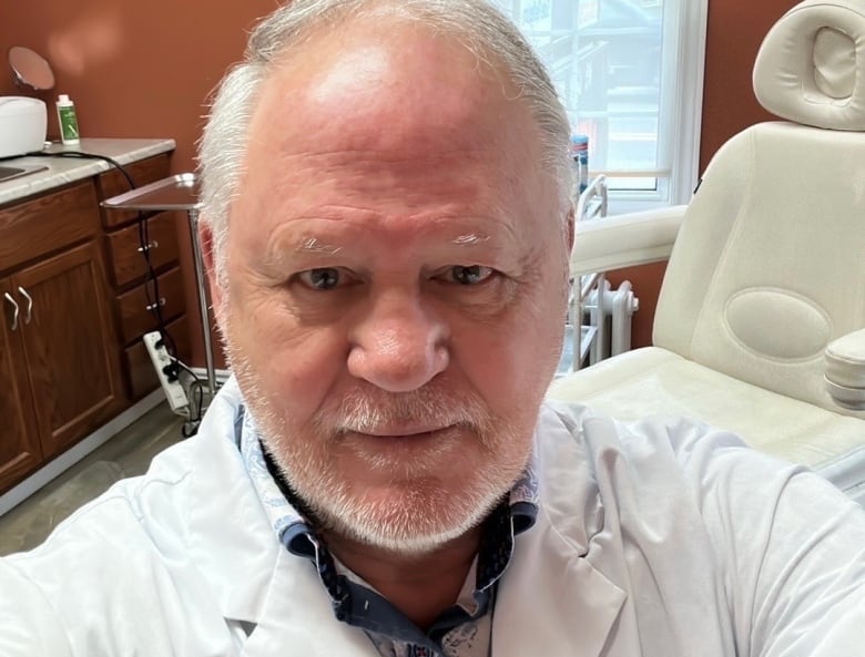 Podiatrist Norman Kew stares at the camera.  His podiatry clinic appears behind him. 