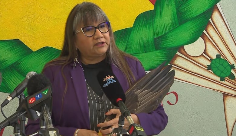 A woman with long hair holds and eagle feather while standing at a podium.