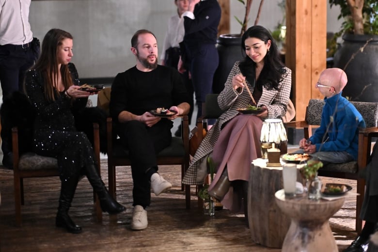 Four people sit around on chairs eating and talking. 