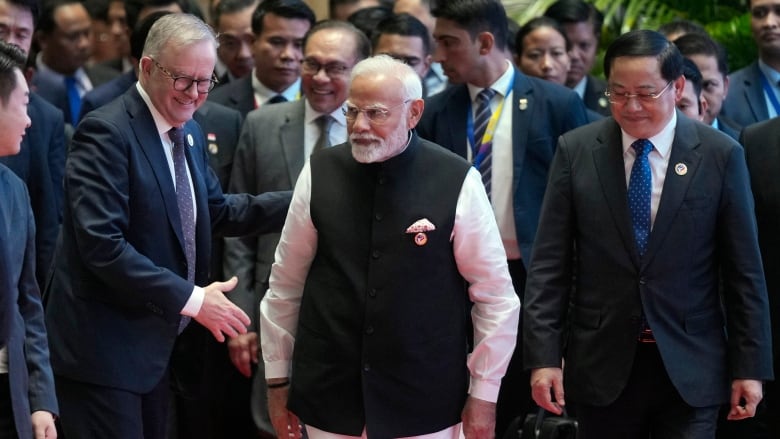 Two men walk together in front of a crowd.