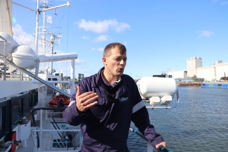 A man waves his hand as he is standing on the deck of a sail boat