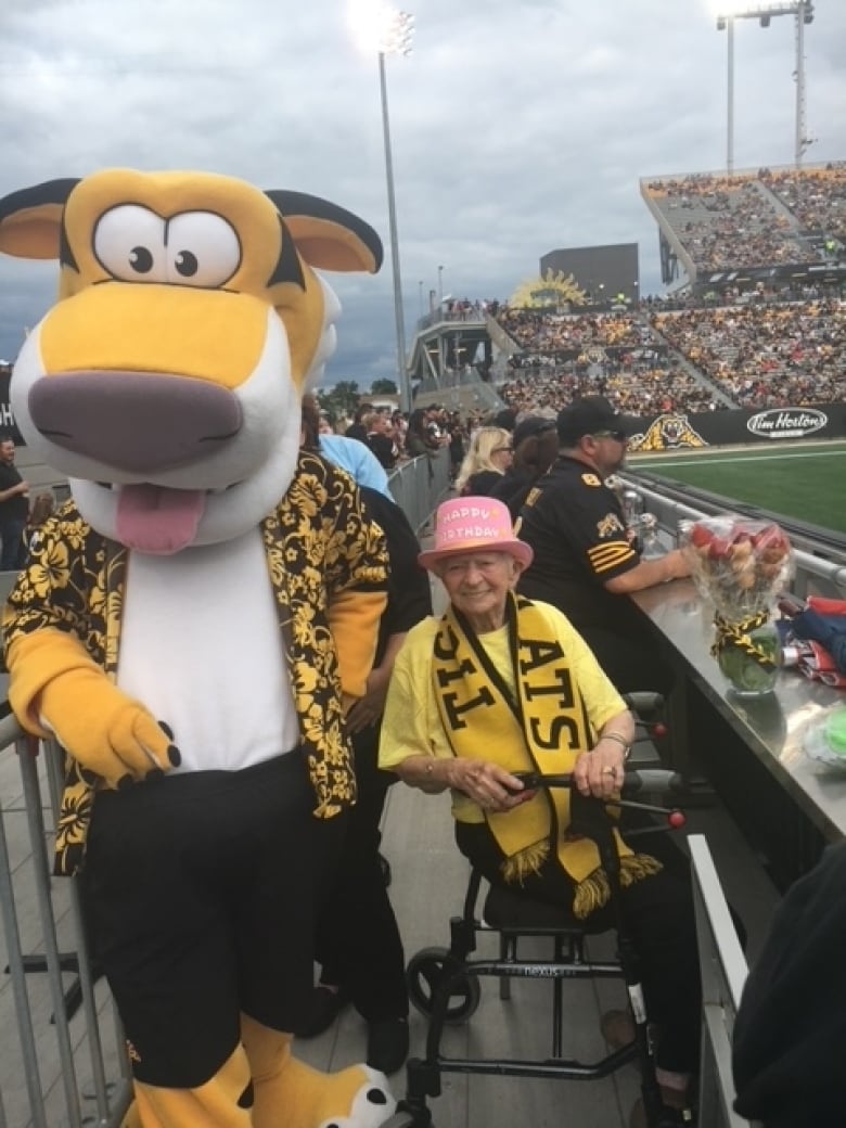 An elderly woman smiles for the camera next to a tiger mascot.