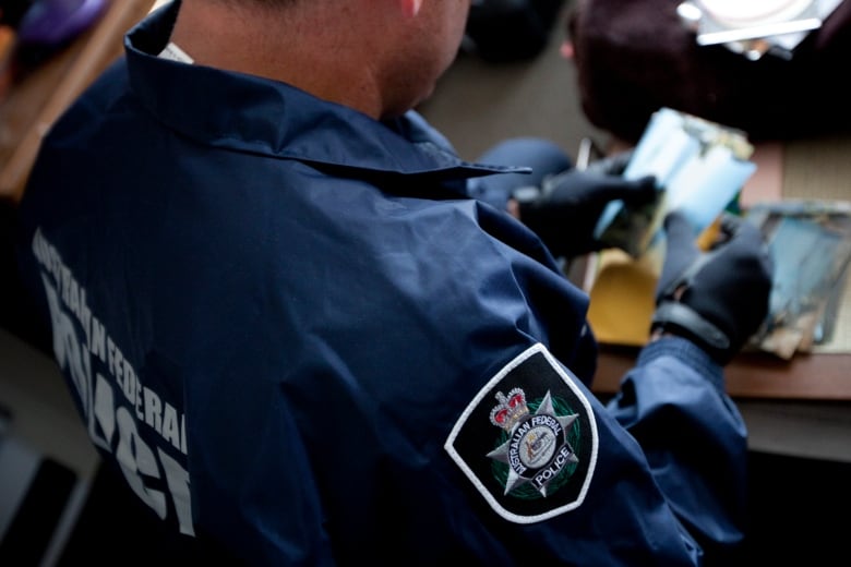 A man in a jacket labeled 'Australian Federal Police' examines evidence, while wearing a pair of black gloves.  