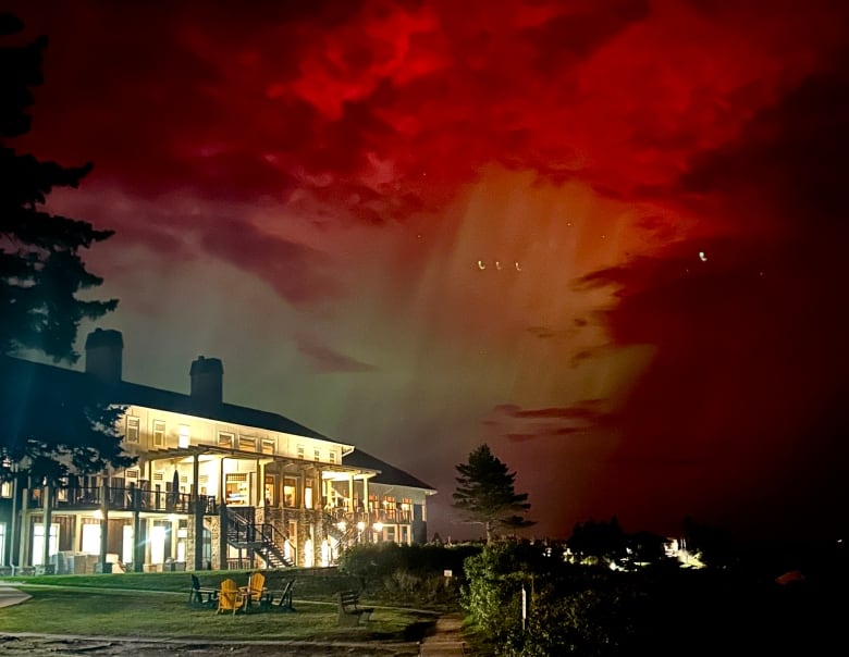 A resort building is shown lit up with lights against a backdrop of a night sky with red northern lights.