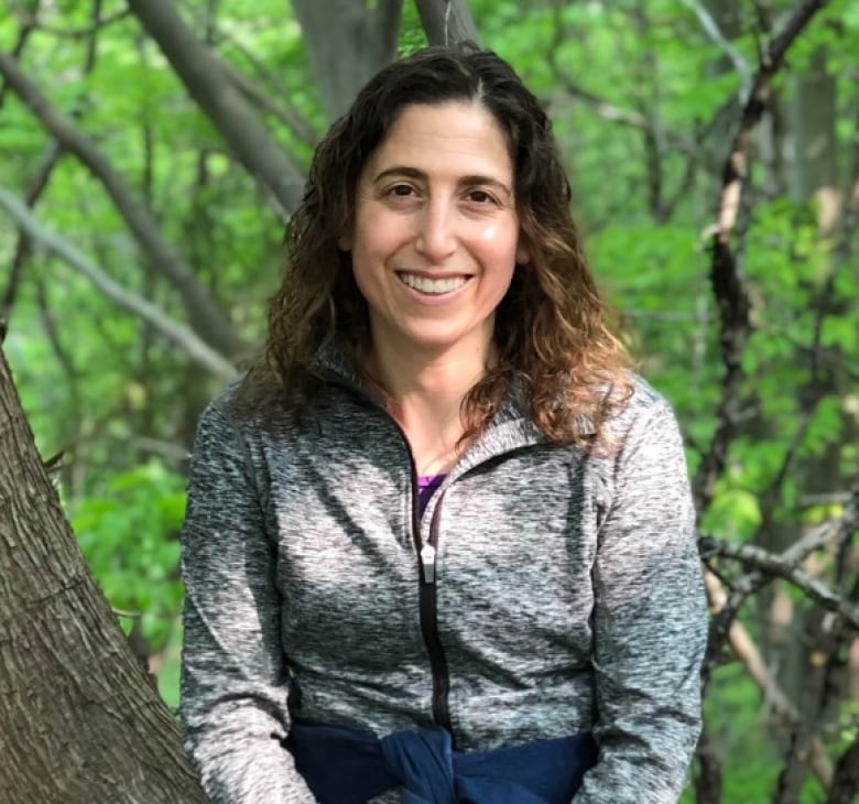 A woman in athletic apparel poses for a photo while sitting on the trunk of a tree.